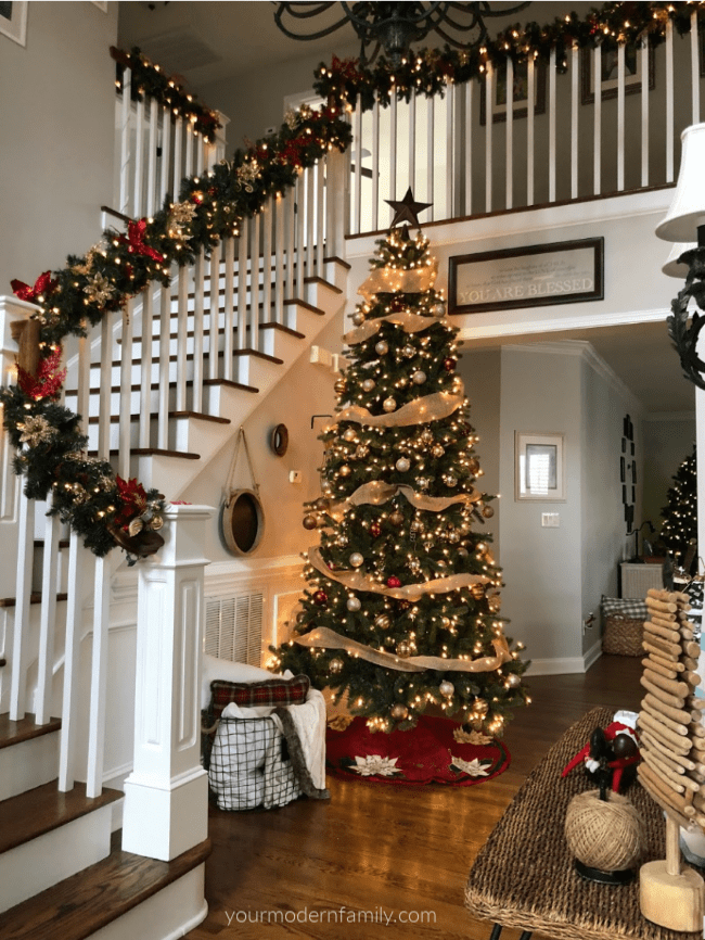 A decorated Christmas tree with decorated stair case beside it. 