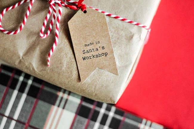 A close up of a brown paper package tied with red and white ribbon with a gift tag attached.