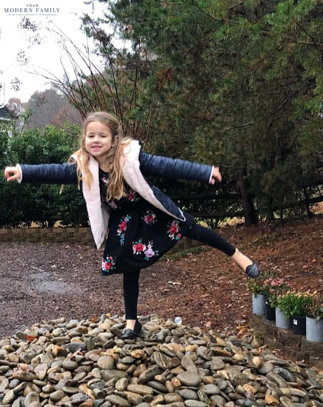 A little girl balancing on one foot with her arms extended on a pile of rocks.
