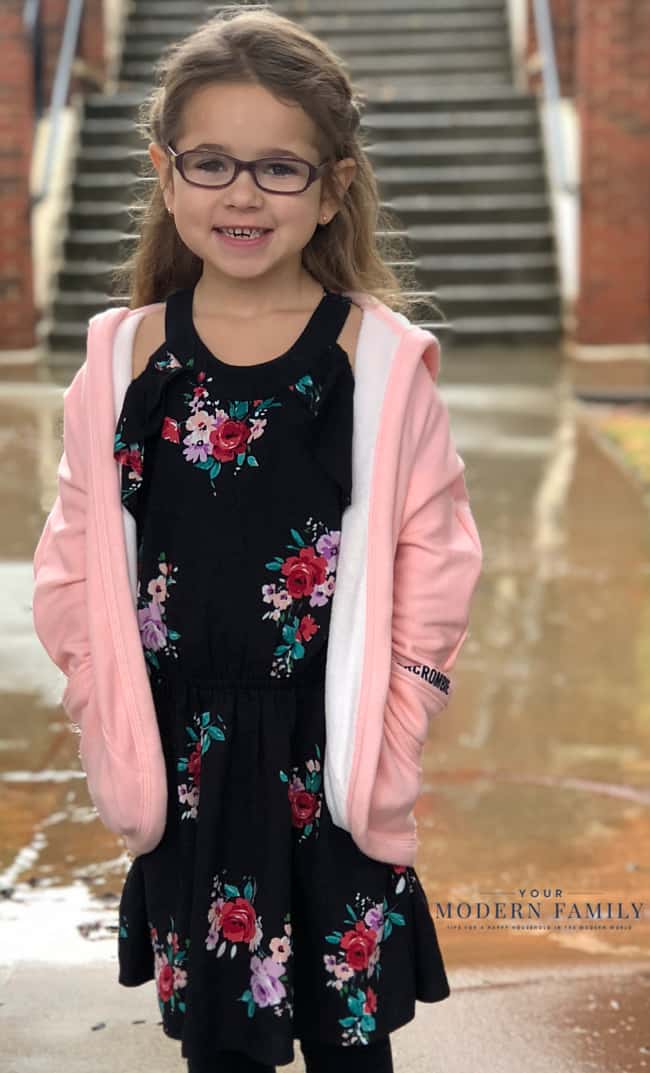 A little girl posing for a picture wearing a flower dress and a pink jacket.