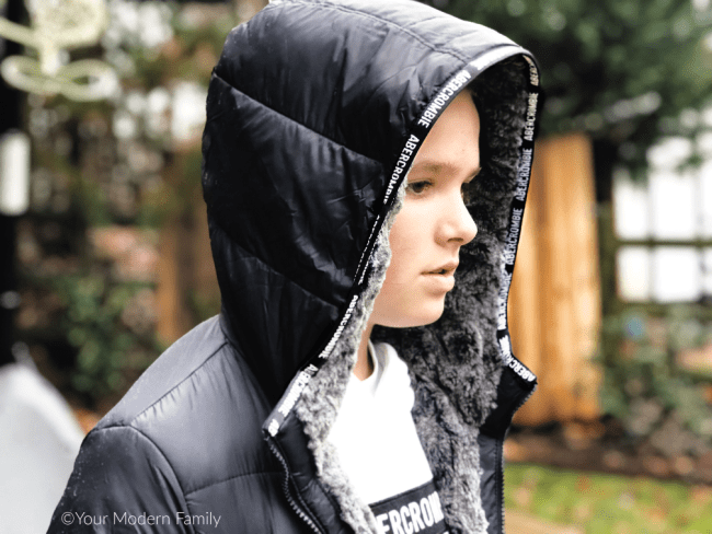 A side picture of a boy wearing a black hooded jacket.
