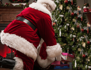 Santa Claus placing gifts under a tree.