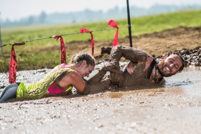 Two people crawling through a mud pit.