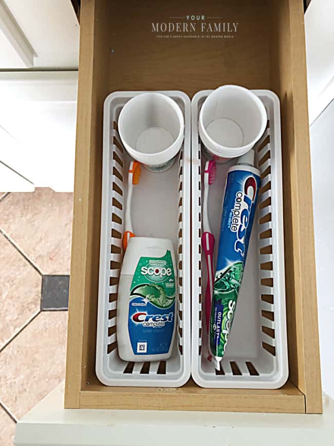 An open drawer with tooth paste, tooth brush and a disposable cup in a plastic container.