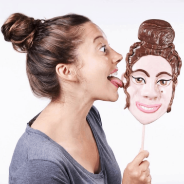 A woman licking a giant lollipop of her face.