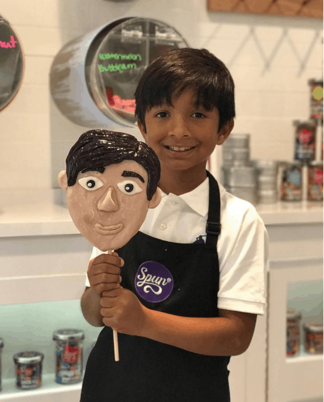 A boy holding a giant look a like lollipop of is face.