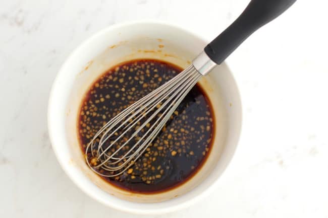 A white bowl with dark brown sauce in it with a whisk resting in the bowl.