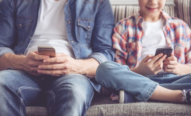A close up of a man and a boy sitting in a chair looking at a cell phone