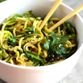 A white bowl with zucchini noodles in it with chopsticks.