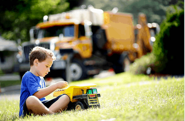 A young boy sitting on the ground playing with a dump truck.