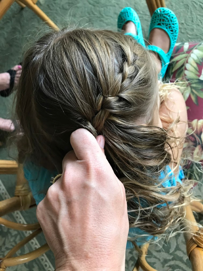 A person braiding a little girl\'s hair.