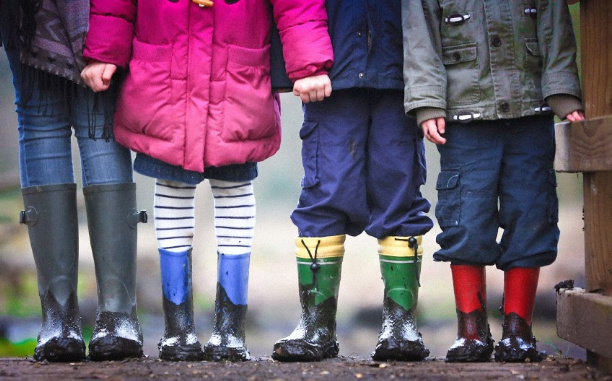 A group of kids posing for the camera wearing rain boots.