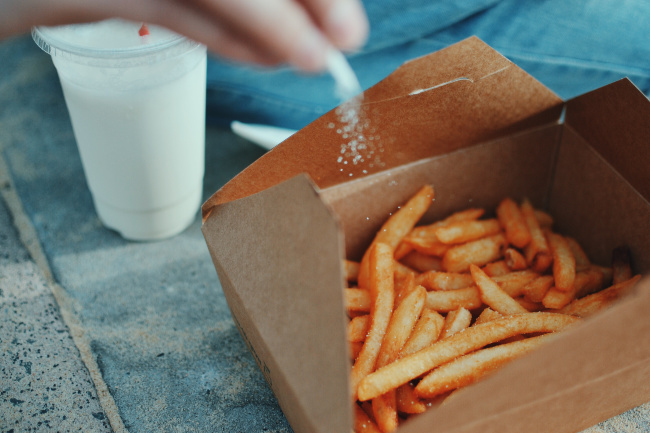 A close up of a tray of french fries with salt being poured on them.