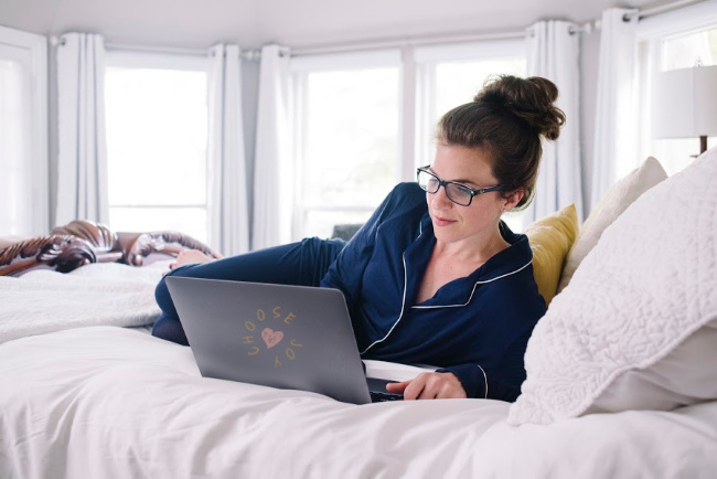 A woman using a laptop computer sitting on top of a bed