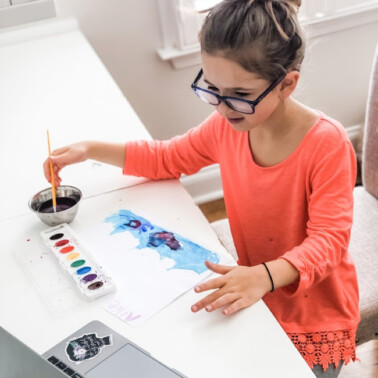 child painting sitting at a table using a laptop